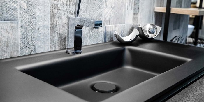 Ein elegantes, schwarzes Spülbecken mit einem modernen Wasserhahn und einer stilvollen Wandverkleidung aus Holz.