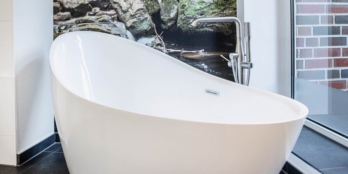 In einem stilvollen Badezimmer befindet sich eine moderne Badewanne, die durch ihre geschwungene Form besticht und viel Licht erhält.
